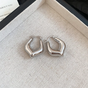Macro shot of silver minimalist V-shaped huggie earrings on beige textured tray