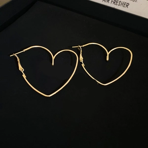 Close-up of minimalist golden heart-shaped metal earrings on black velvet tray