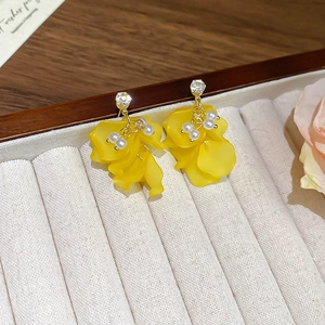 Dettaglio di orecchini a fiore gialli con perle e zircone su velluto beige liscio