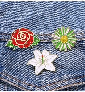 Detailed view of red rose and white lily enamel pins pinned on blue denim fabric