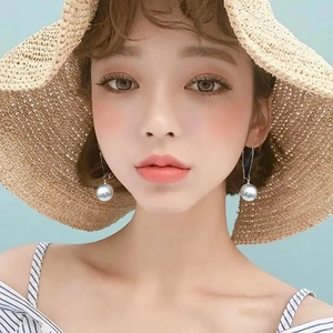 Nahaufnahme großer runder Perlenohrringe mit Strohhut für einen sommerlichen Look