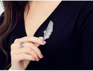 Close-up of sparkling zircon feather brooch and silver floral ring on black sweater