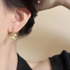 Close-up of 18k gold plated rocking horse charm hoop earrings on model's ear