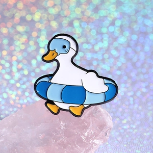 Cute enamel duck pin with swim goggles and ring against a dreamy bokeh background