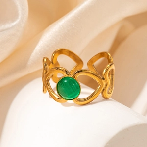 Détail d'une bague coeur dorée évidée avec pierre verte sur soie et pierre élégante