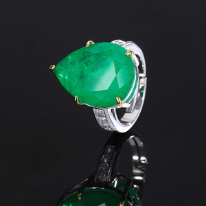 Detailed close-up of a pear-cut emerald zircon ring with brilliant sparkle on black background