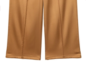 Detail of bronze satin wide-leg pants showing the smooth fabric and vertical seam line
