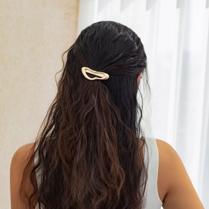 Detail of a golden irregular geometric hair clip styled on dark brown wavy hair