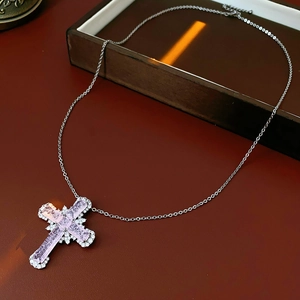 Close-up of pink zircon cross pendant on silver chain over luxury leather background