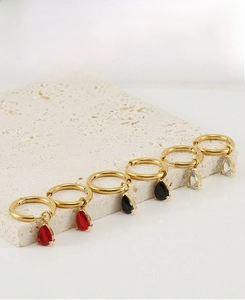 Macro view of three pairs of gold hoop earrings with red, black, and clear zircon teardrops