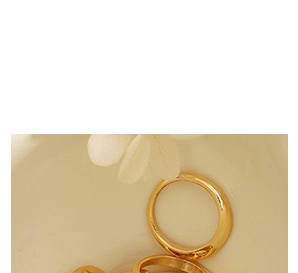 Close-up of gold ring set with minimalist and wavy designs on a ceramic dish with dried petals