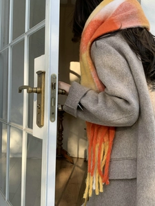 Close-up of orange gradient knit scarf with fringe detail worn over a beige coat