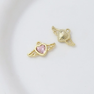 Macro detail of gold-tone winged heart charm with pink zircon inlay on white background