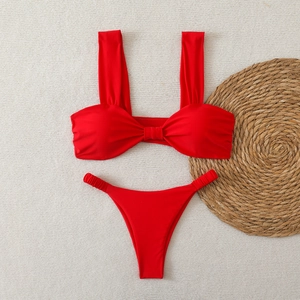 Bikini bandeau rouge avec nœud décoratif disposé à plat sur fond de plage texturé