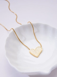 Detail of gold heart pendant with marble inlay on sleek snake chain in a shell dish