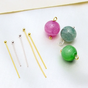 Gold and silver ball head pins for DIY jewelry making shown with colorful beads on white cloth