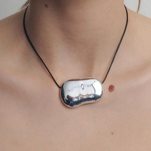 Close-up of minimalist silver irregular bean pendant on a black cord necklace