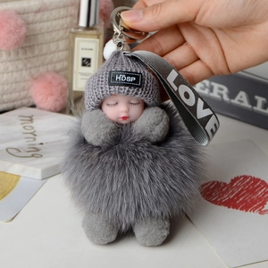 Detail of grey fox fur ball keychain with sleeping baby doll and grey knit cap