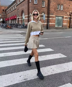 Outdoor street style showing a khaki V-neck knitwear over a white shirt and pleated skirt