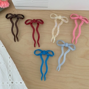 Flat lay of six colorful bow-shaped U-shaped hair clips on a light wood surface