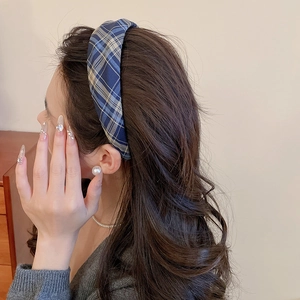 Detail view of a thick blue and brown plaid fabric headband on dark wavy hair
