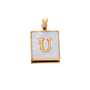 Macro detail of golden square pendant with letter U inlay and white shell texture