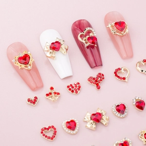 Red heart nail art charms with bow designs and rhinestones on pink background