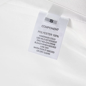 Détail de l'étiquette de lavage blanche indiquant la taille S et 100% de composition polyester