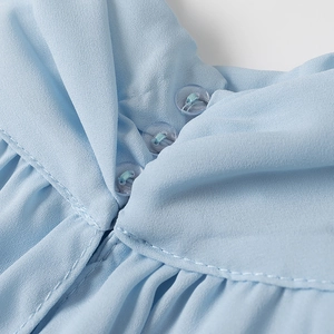 Detail view of light blue chiffon collar featuring delicate pleats and a round button