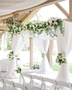 Close-up of elegant white chiffon arch draping with floral rose and greenery decor