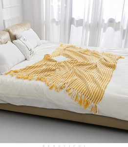 Detail of yellow and white striped knit blanket with fringe tassels on white bedding