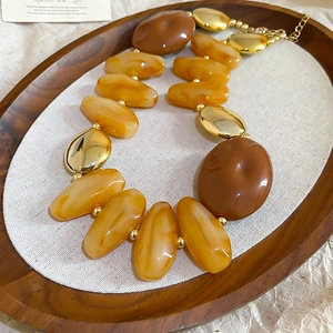 Detail view of amber acrylic and gold oval beaded necklace on a wooden tray with fabric