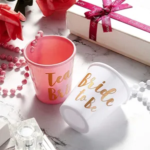 Pink and white Bride to Be party shot glasses with gold lettering on marble background