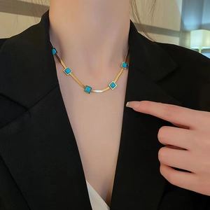 Collana a catena piatta dorata con pietre turchesi quadrate indossata da una modella