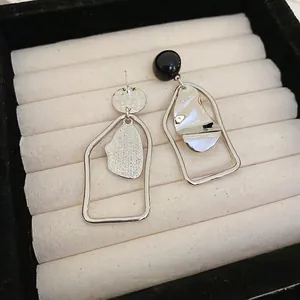Asymmetric silver and black geometric earrings on a beige velvet jewelry display