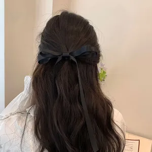 Detail of a large black satin bow hair clip with long ribbons on wavy brown hair