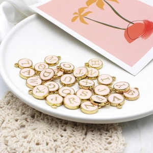 Pink enamel alphabet charms with gold metal edges on a white ceramic plate