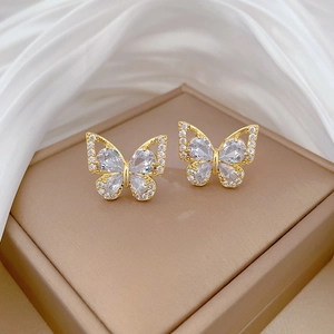 Macro view of gold butterfly stud earrings with zircon inlay on luxury satin backdrop