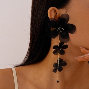 Dettaglio di orecchini pendenti con fiori in chiffon nero indossati da una modella