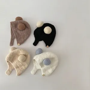 Plush baby earflap hats with dual pompoms in four neutral colors for winter warmth