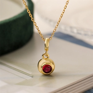 Close-up of a gold-plated circular pendant necklace with a central red zircon stone