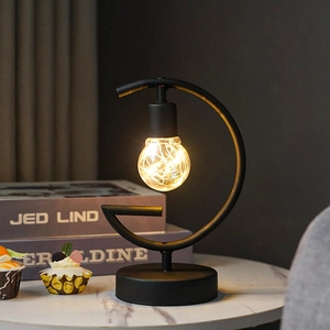 Detail of G-shaped black iron lamp with warm LED copper wire bulb on marble table