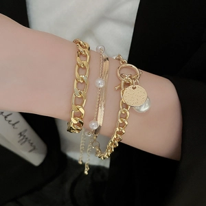 Detail of layered gold bracelet set featuring cable, snake chain, and white pearls