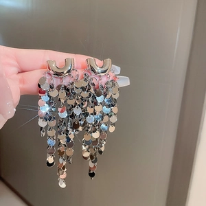 Detailed close-up of long U-shaped silver cluster sequin fringe earrings held by hand
