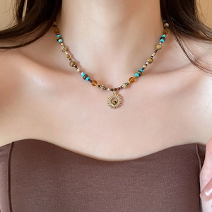 Close-up of bohemian beaded necklace with gold sun pendant worn on model's neckline