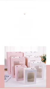 Détail de sacs cadeaux en papier rose et blanc avec fenêtre et poignées en corde de tailles