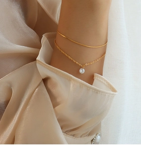 Close-up of double-layered gold bracelet with zircon pendant on a model's wrist