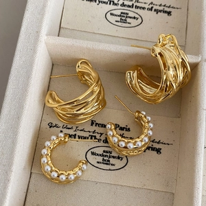 Golden multi-layer metal C-shaped hoop earrings and white pearl studs in a jewelry box