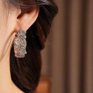 Detailed view of silver wire-wrapped bird nest earrings shown on a model ear