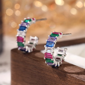 Macro shot of silver C-shaped hoop earrings featuring colorful baguette cut zircons